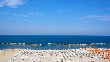 Una spiaggia con file di lettini e ombrelloni, un cielo azzurro limpido e il mare sullo sfondo.