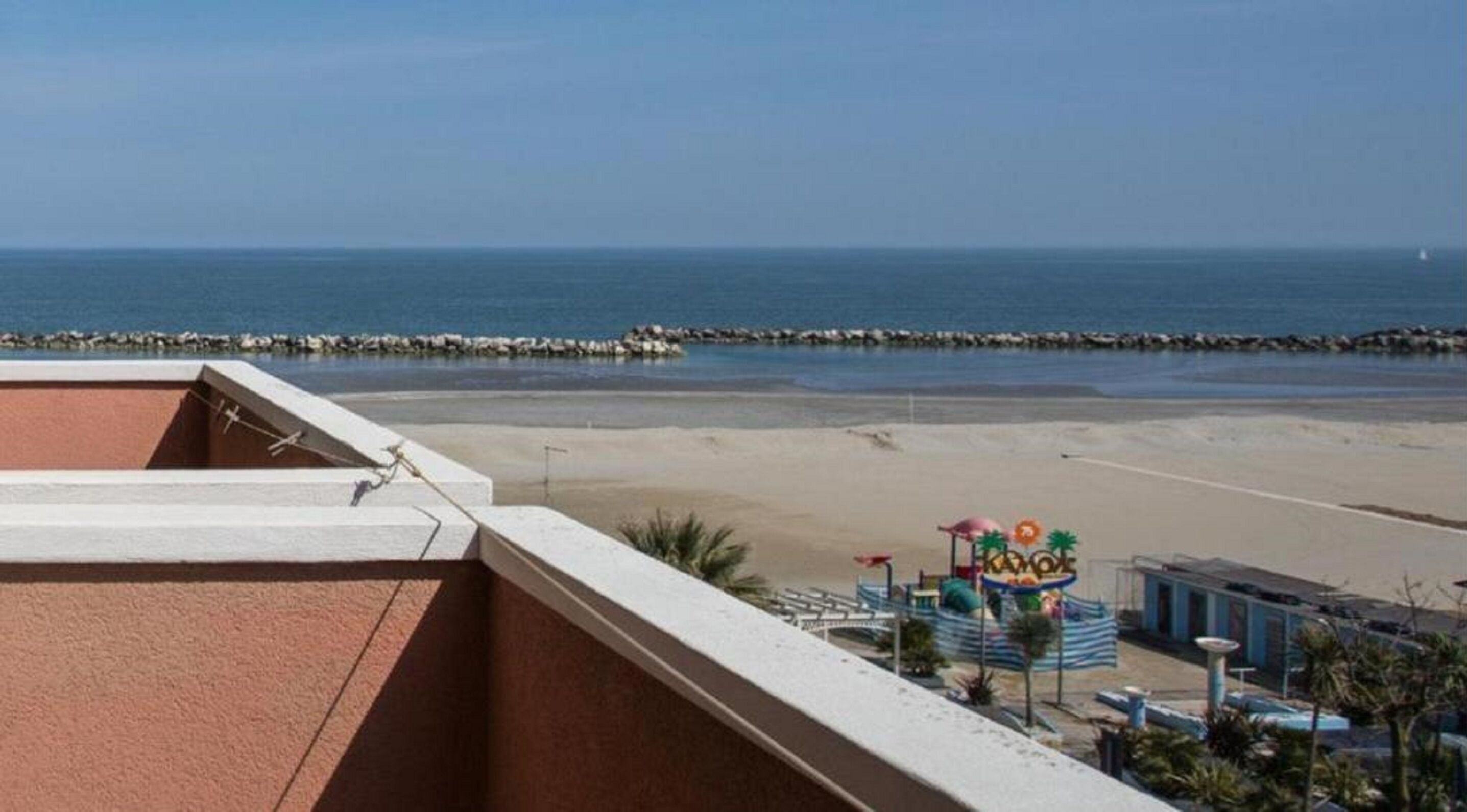Vista a la playa desde un balcón con zona de piscina y un cartel que dice "KOMOLE".