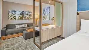 Habitació d'hotel moderna amb llit, sofà, escriptori i obra d'art a les parets.