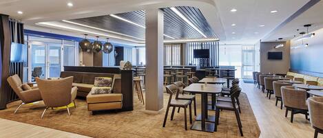A modern hotel lobby with a seating area, a reception desk, and a dining section.