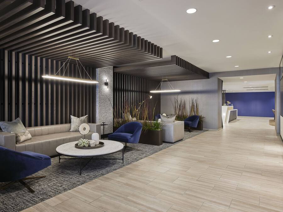 A modern lobby with a reception desk, seating area with sofas and chairs, and a patterned ceiling.