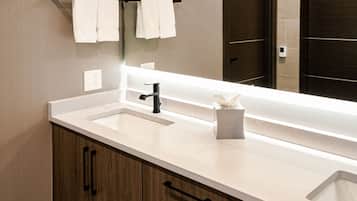 A modern bathroom with a white sink, black faucet, and wooden cabinets. There are two white towels hanging on a black towel rack above the sink.
