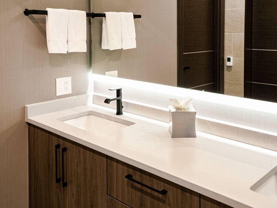 A modern bathroom with a white sink, black faucet, and wooden cabinets. There are two white towels hanging on a black towel rack above the sink.