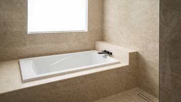 Ein modernes Badezimmer mit einer freistehenden Badewanne, einem Fenster und beige gefliesten Wänden.