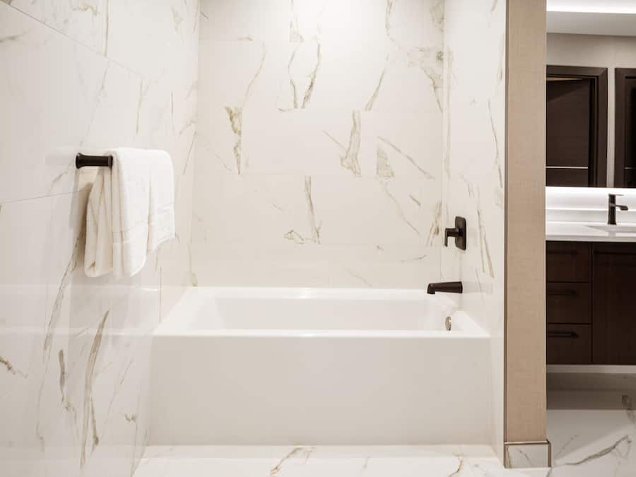 A modern bathroom with a marble wall, a white bathtub, and wooden cabinets.