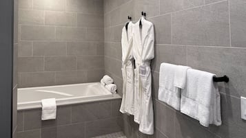 A modern bathroom with a bathtub, two white robes hanging on hooks, and a towel rack with folded towels.
