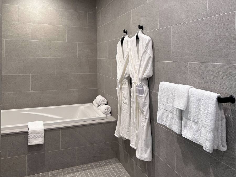 A modern bathroom with a bathtub, two white robes hanging on hooks, and a towel rack with folded towels.