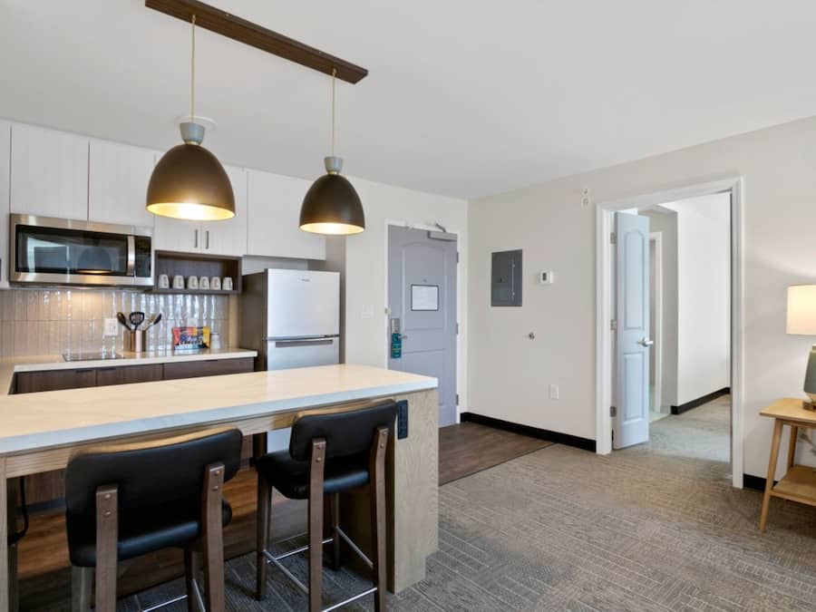 A modern kitchen with a central island, bar stools, pendant lighting, and a microwave.
