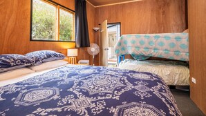 A room with a large bed, a smaller bed, a standing fan, and a window with curtains.