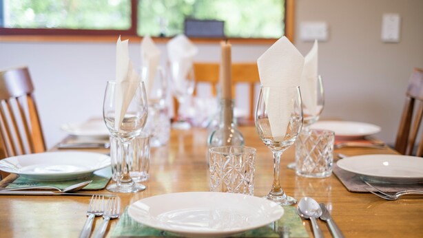 A dining table set with plates, cutlery, and glassware, with a candle and napkin on the table.