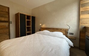 Een slaapkamer met een houten bedframe, een garderobe met spiegel en een nachtkastje met lamp.