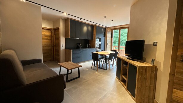 Una cocina moderna con armarios oscuros, un comedor con mesa y sillas de madera, y un televisor sobre un mueble de madera.