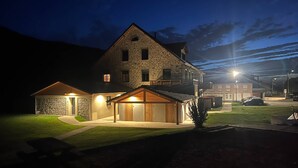 A large stone building with a prominent central tower, a covered porch, and a well-lit entrance. - Rental of 12 gîtes and 1 chalet that can accommodate 2 to 10 people. (Rochesson)