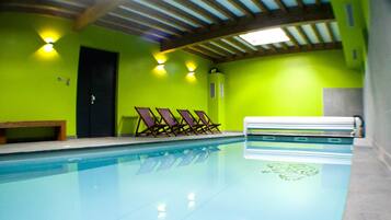 Una piscina con una panchina e lettini prendisole, una porta e un soffitto con travi e luci in legno.