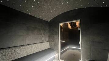 Een moderne spa ruimte met een bankje, een glazen deur naar een stoomruimte en een plafond met kleine lampjes.