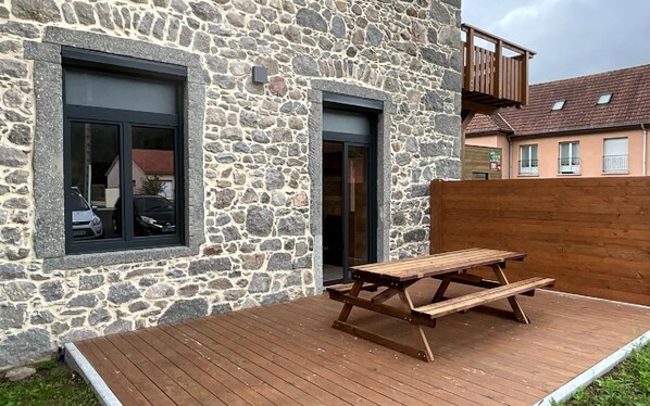 A stone building with two windows and a wooden deck with a picnic table.