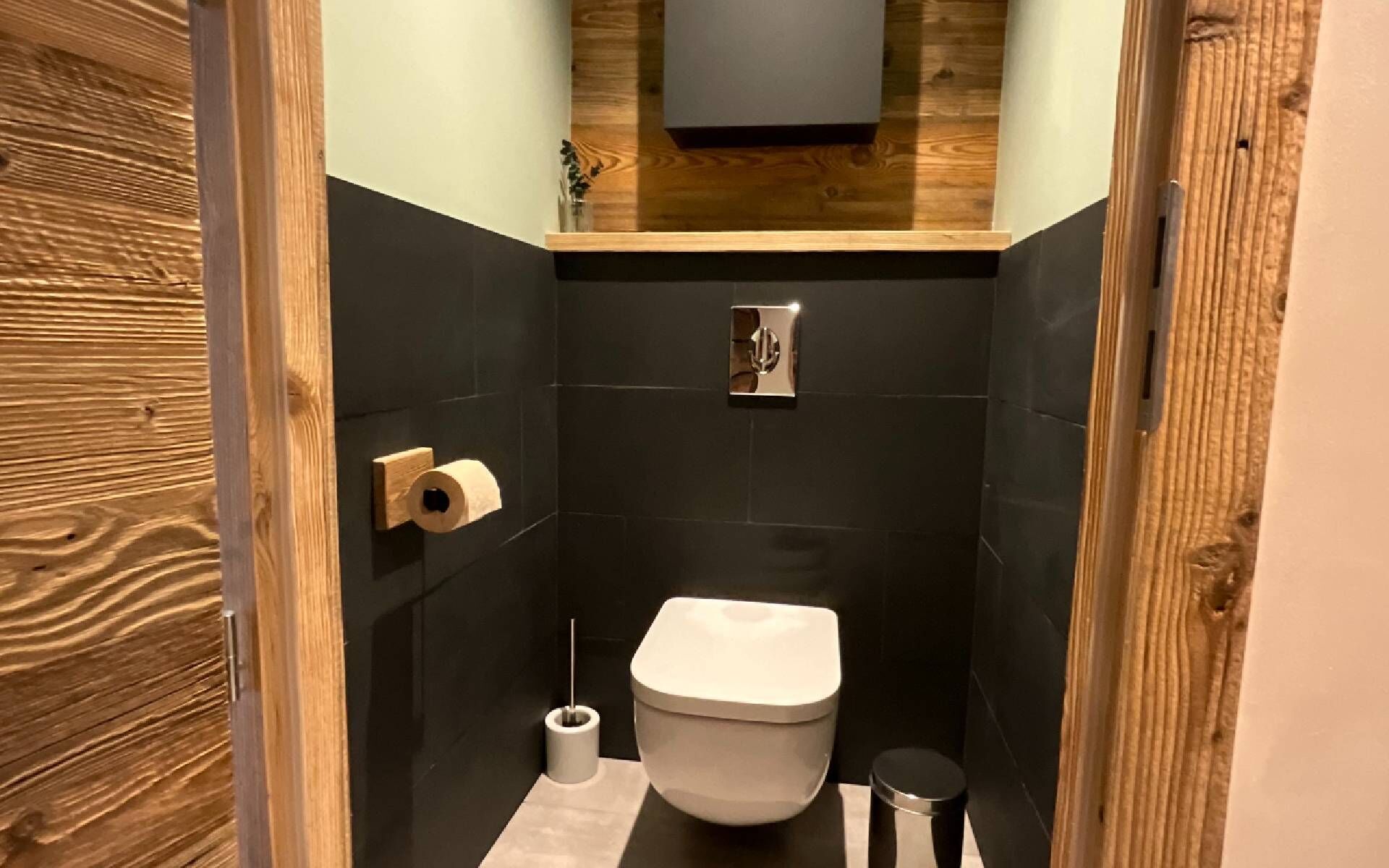 A compact bathroom with a toilet, a small trash bin, and a toilet paper holder.