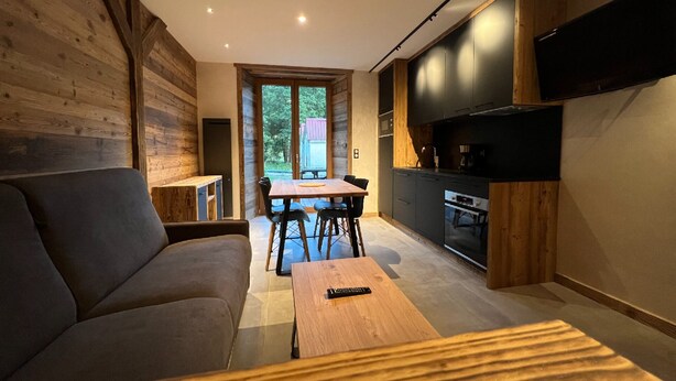 A modern living room with a sofa, a wooden coffee table, and a dining area with chairs and a table. - Rental of 12 gîtes and 1 chalet that can accommodate 2 to 10 people. (ROCHESSON)