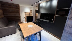 A modern kitchen with dark cabinets, a wooden dining table, and a grey sofa. - Rental of 12 gîtes and 1 chalet that can accommodate 2 to 10 people. (Rochesson)