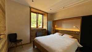 A bedroom with a wooden headboard, a bed with white bedding, a desk with a chair, and a window with a view of trees. - Rental of 12 gîtes and 1 chalet that can accommodate 2 to 10 people. (ROCHESSON)