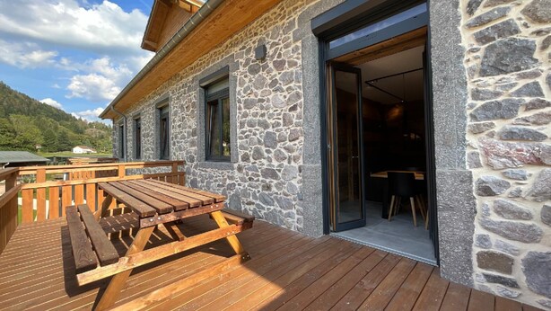 A stone building with a wooden deck and a table. - Rental of 12 gîtes and 1 chalet that can accommodate 2 to 10 people. (ROCHESSON)