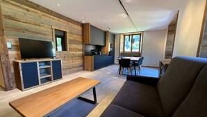 Una sala moderna con una pared de acento de madera, un televisor de pantalla plana, un sofá y una zona de comedor con mesa y sillas.