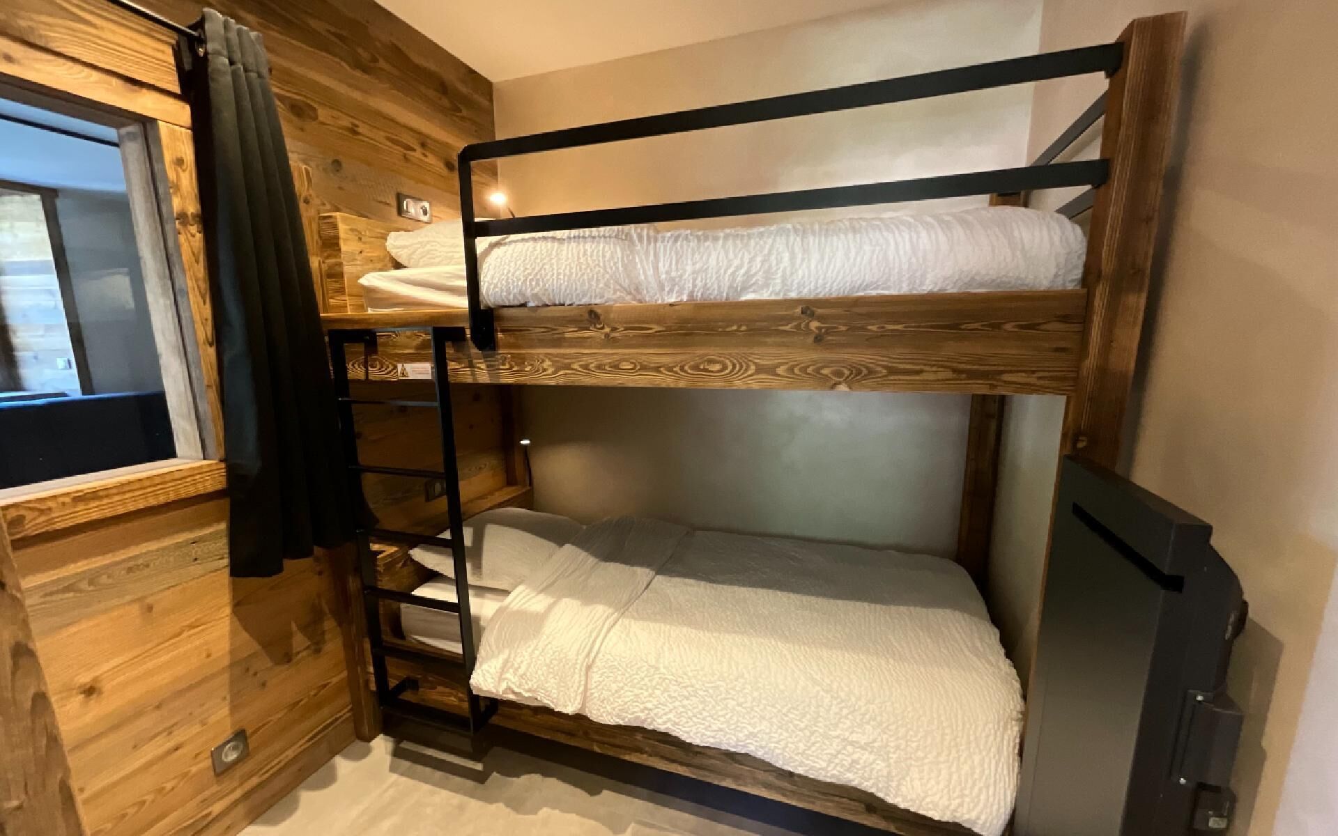 A bunk bed with a wooden headboard, a window with curtains, and a small shelf.