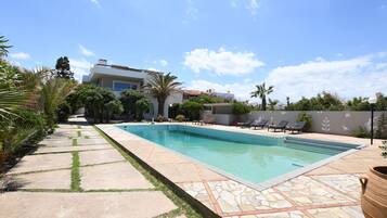 A swimming pool with a tiled deck, surrounded by palm trees and lounge chairs.