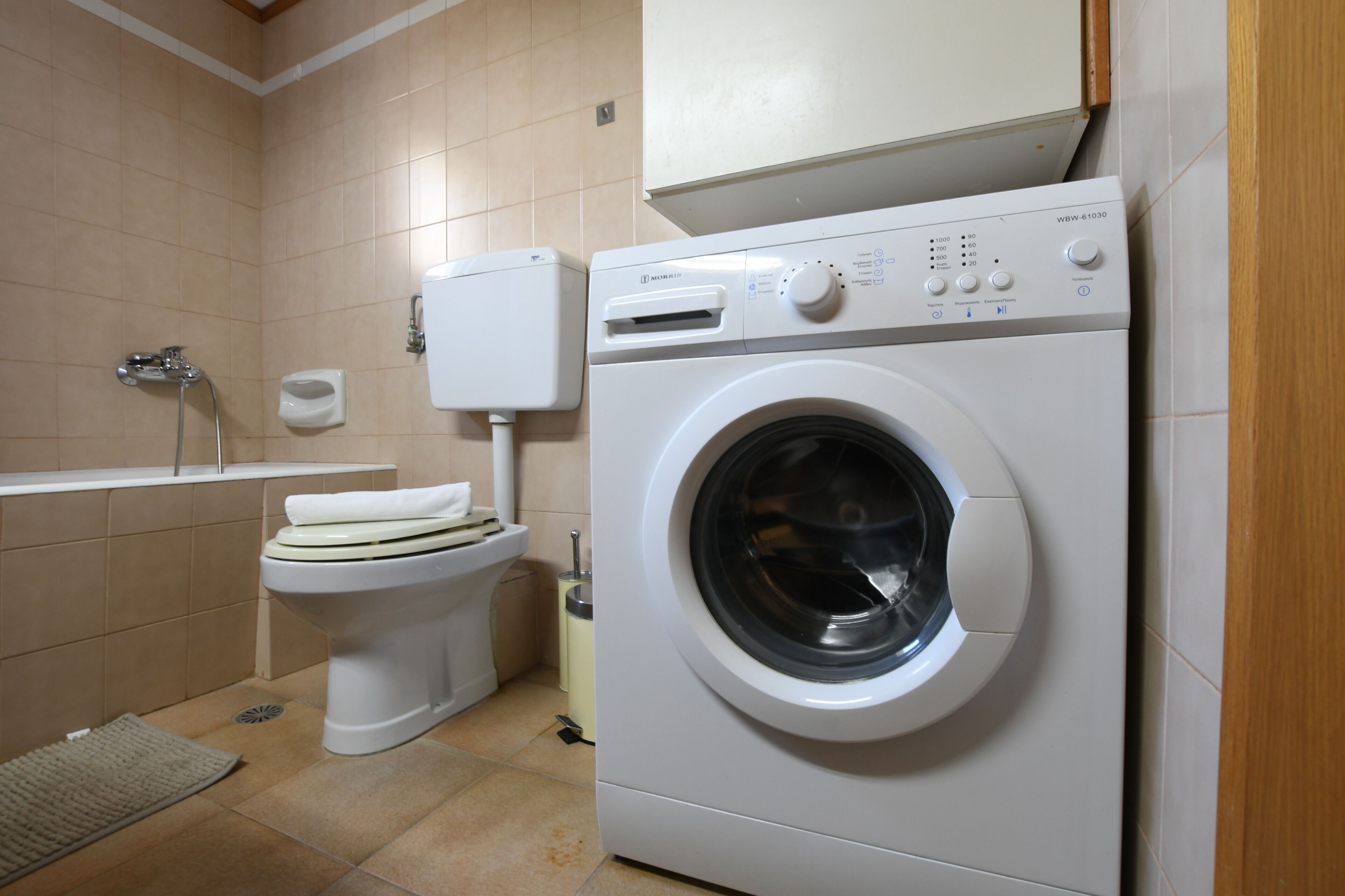 A compact bathroom with a washing machine, toilet, and a shower.