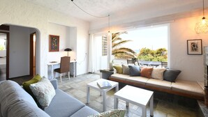 A living room with a sofa, a dining table, and a bench. There is a view of the outdoors through a large window. - Villa Breath of the Sea (Hersonissos)