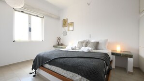 A bedroom with a bed, bedside tables, a window, and wall decorations. - Villa Breath of the Sea (Hersonissos)