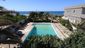 A swimming pool with a view of the sea, surrounded by palm trees and a modern building. - Villa Breath of the Sea (Hersonissos)