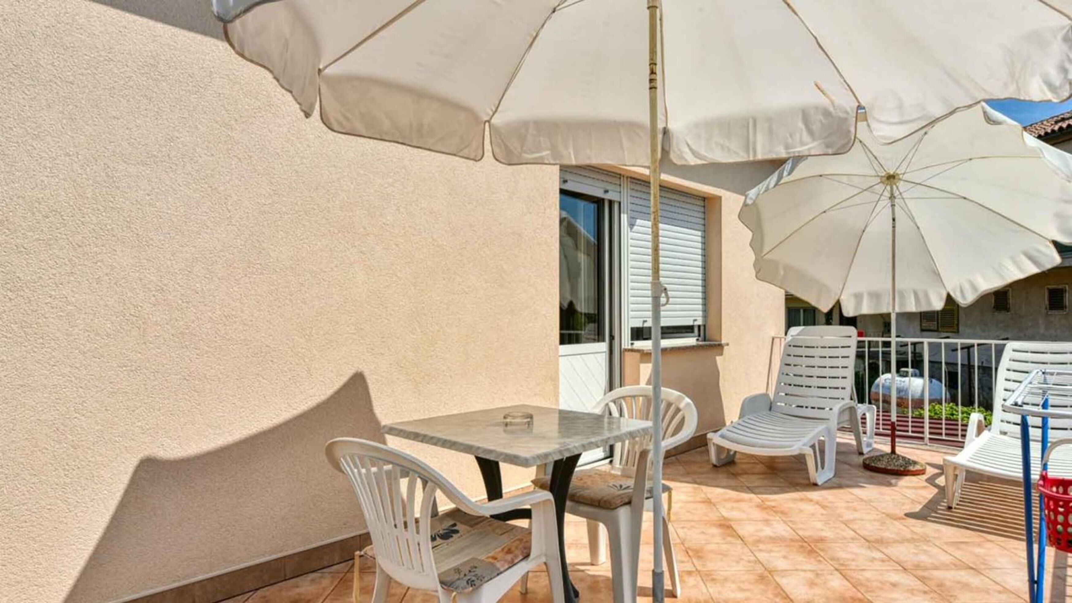 Une terrasse avec une table et des chaises, un grand parasol et un espace au bord de la piscine équipé de chaises longues.