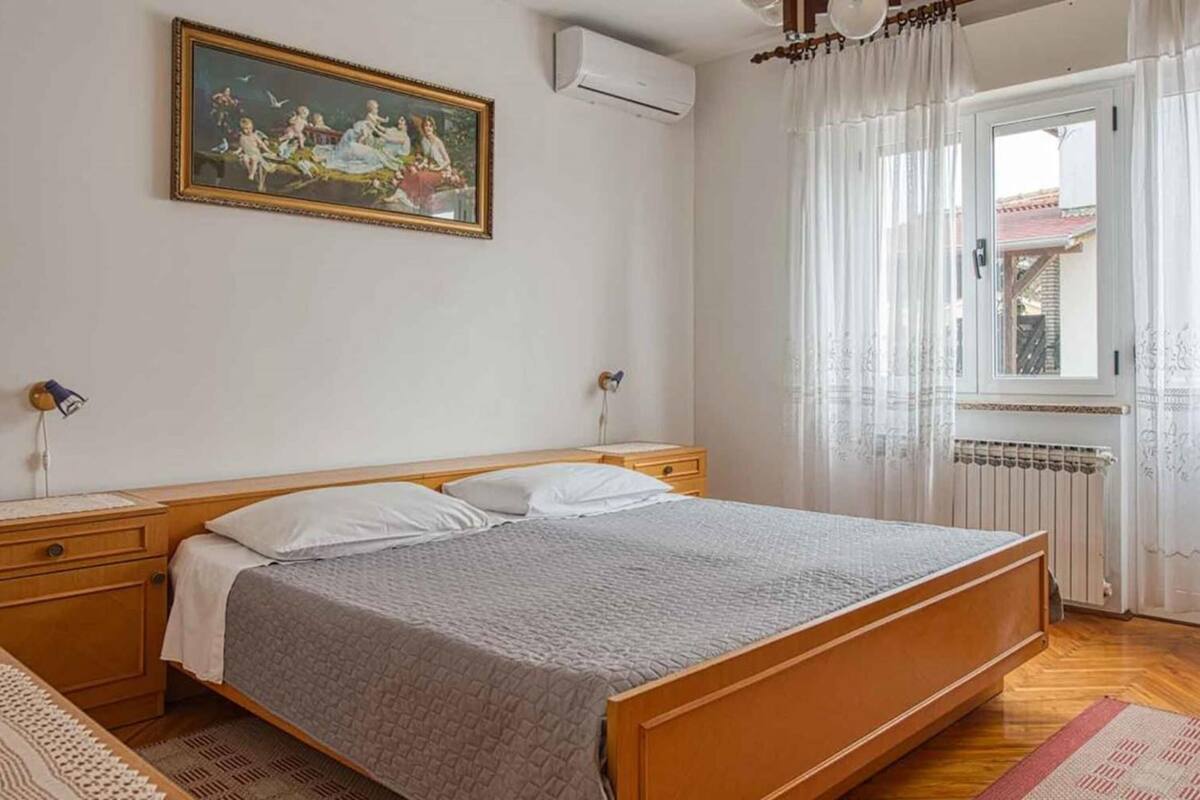 A bedroom with a wooden bed, a nightstand, a lamp, a painting on the wall, and a window with curtains.