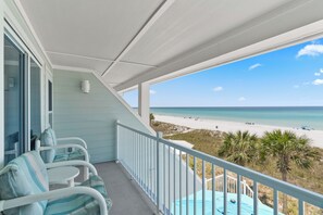 Un balcon avec vue sur une plage, une piscine et un espace salon avec des chaises.