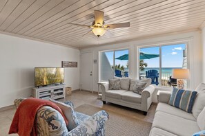 Un salon équipé d’un ventilateur de plafond, d’une télévision, d’un canapé et d’une fenêtre donnant sur la plage.