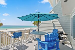 Een balkon met tafel, stoelen en parasol met uitzicht op een strand.