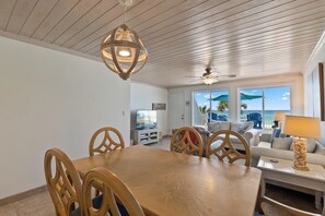 Ein Essbereich mit Holztisch und -stühlen, einem Deckenventilator und Blick auf das Meer durch große Fenster.