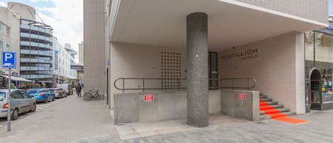 A hotel entrance with a tiled facade, a visible staircase, and a parking sign.