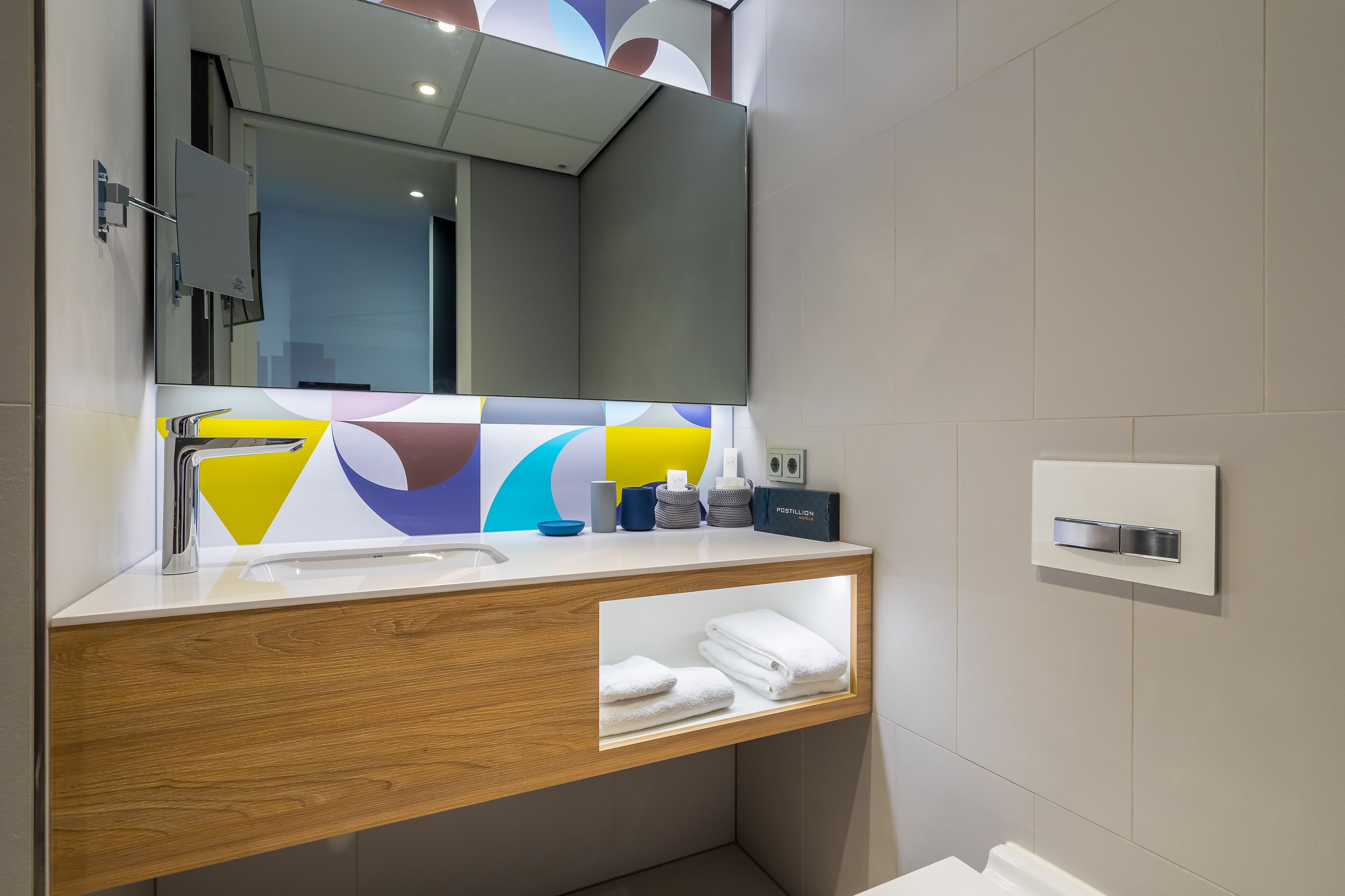 A modern bathroom with a wooden vanity, a large mirror, and a built-in towel rack.