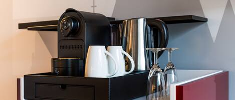 A coffee station with a coffee maker, cups, and glasses on a counter.