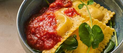 A bowl of ravioli with tomato sauce and spinach.