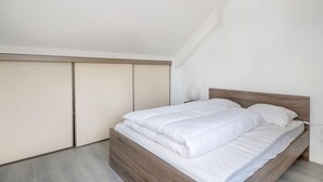 A bedroom with a wooden bed, white bedding, and a closet with sliding doors. - Arzon- house for 2 with great seaview (Arzon)