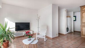 A modern living room with a flat-screen TV, a white chair, a small table, and a potted plant. - Arzon- house for 2 with great seaview (Arzon)