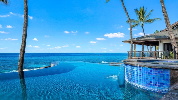 A infinity pool with clear blue water, palm trees, and a view of the ocean. - Summer Deal Kona Oceanfront Estate with Pool Water Slide Guest House (Kauilua Kona)