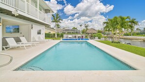 Una piscina con lettini, una zona relax coperta e vista su un edificio residenziale con un balcone.