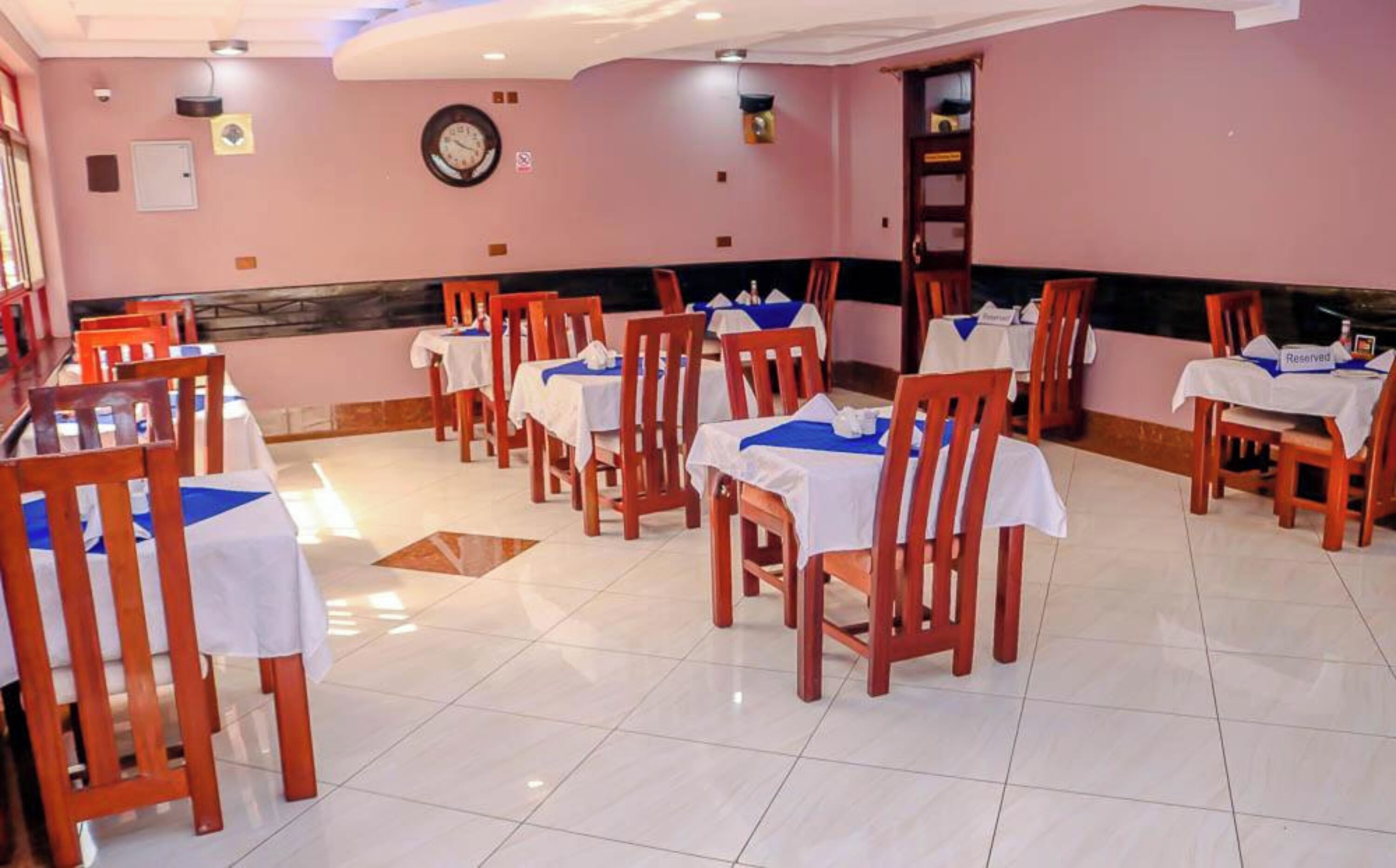 A restaurant with wooden chairs and tables, a clock on the wall, and a tiled floor.