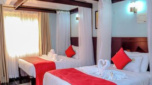 A hotel room with two beds, each with white bedding and red pillows, and a red blanket. The room has a wooden headboard and a large window with curtains. - Davana Hotel (Nairobi)