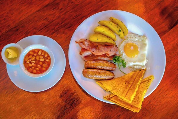 A plate of food including eggs, bacon, sausages, and toast, along with a bowl of beans and a small dish of butter. - Davana Hotel (Nairobi)
