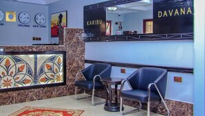 A lobby with a reception desk, two black chairs, a small table, a decorative tile wall, and clocks displaying times from Beijing, New York, and Tokyo. - Davana Hotel (Nairobi)